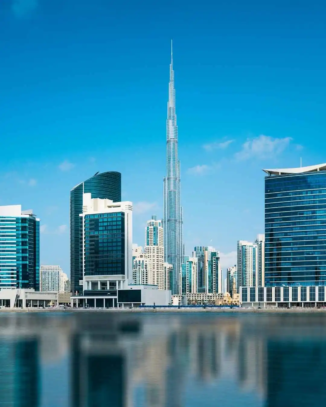 Modern skyline view of property in Dubai with Burj Khalifa and waterfront reflections under blue sky.