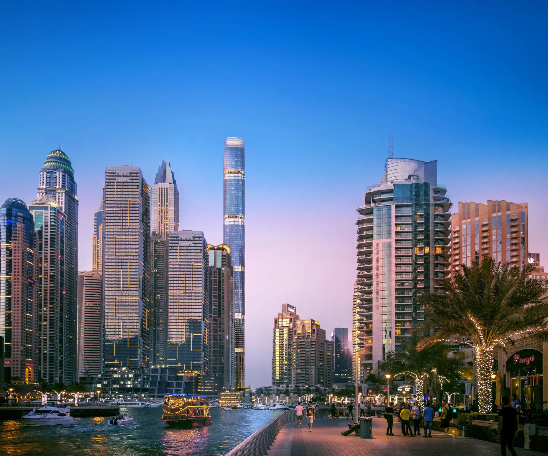 Dubai Marina waterfront at dusk with luxury yachts, high-rises, and Six Senses Residences nearby.