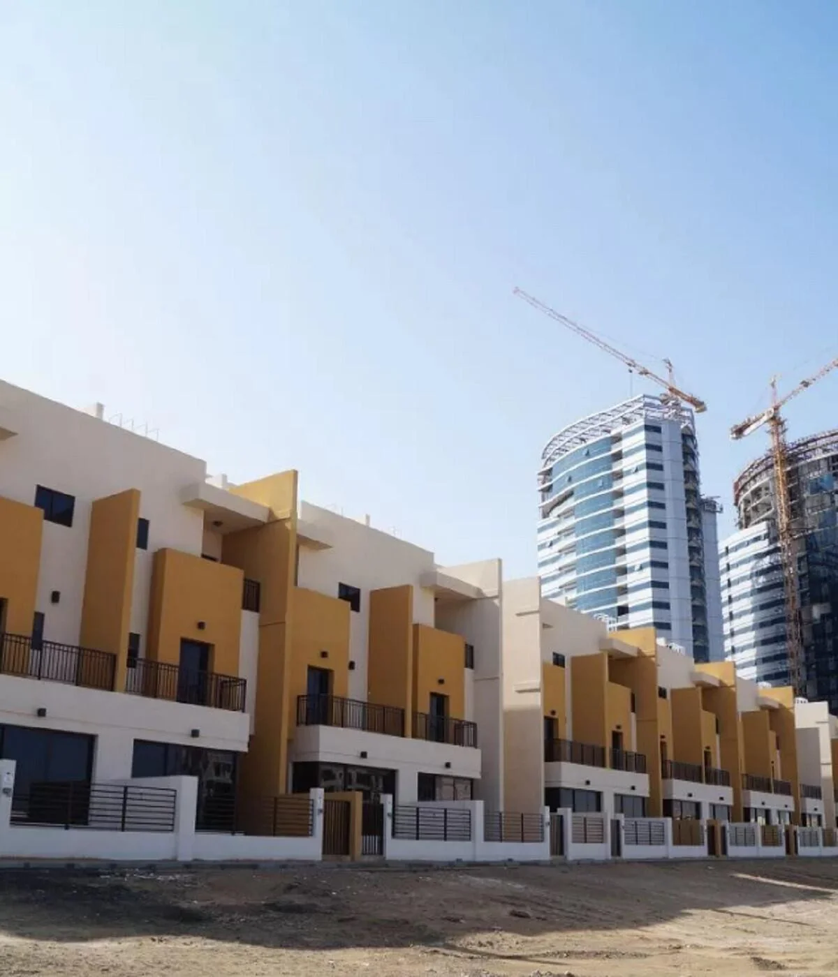 Row of modern yellow-accented townhouses at Lilac Park with nearby high-rise buildings under construction.